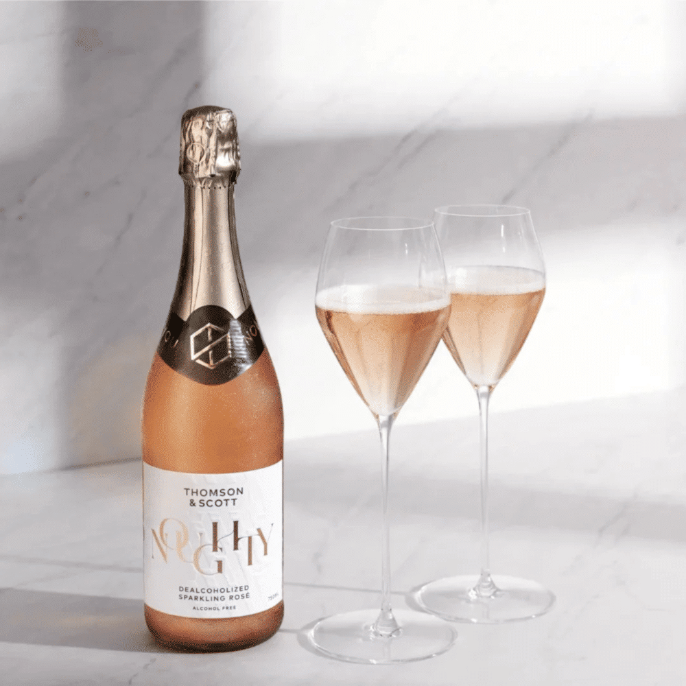 Bottle of Noughty non alcoholic sparkling rosé with two wine glasses in a minimalist setting