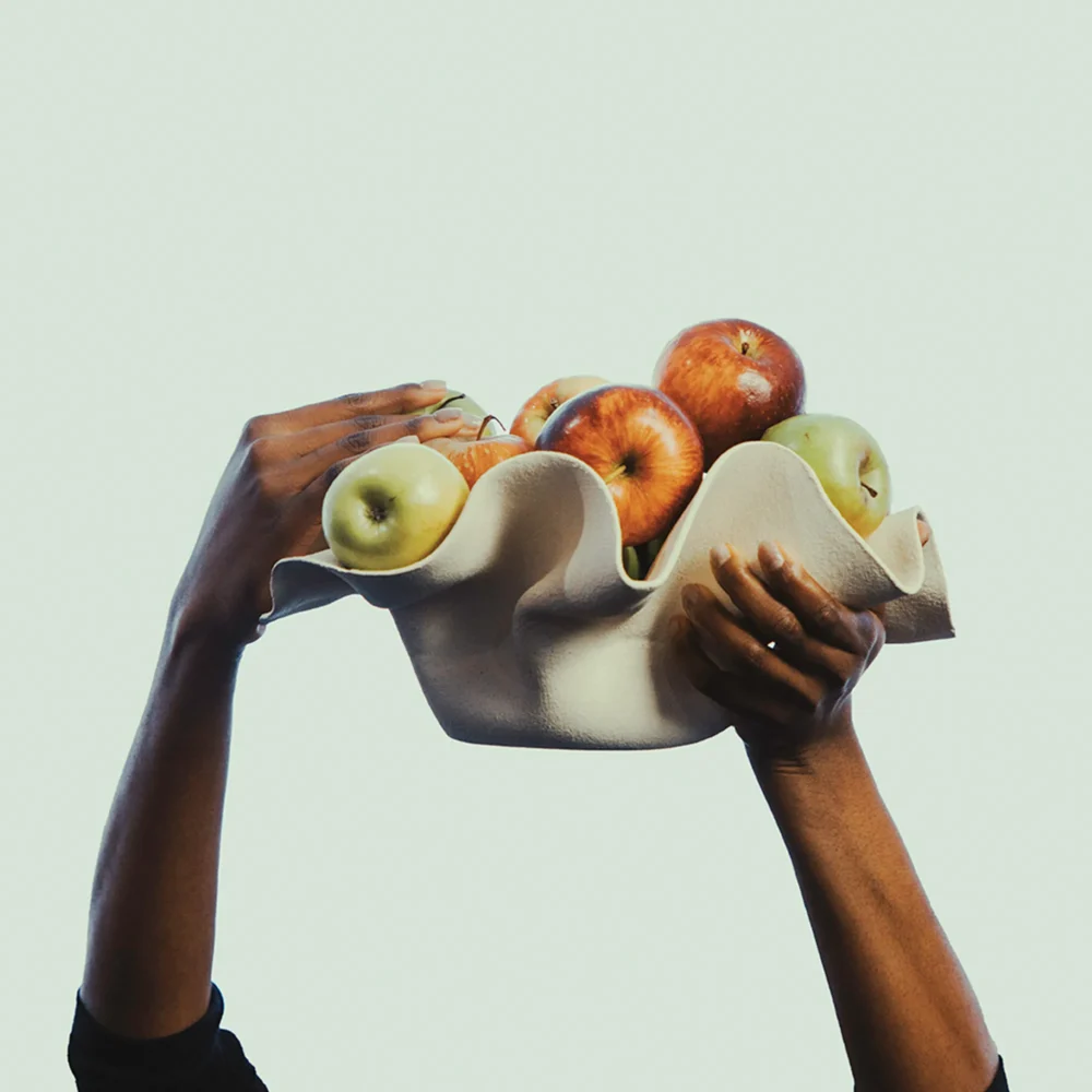 Hands holding a sculptural bowl filled with red and green apples
