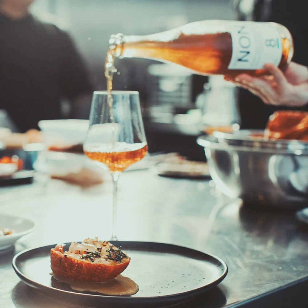 NON8 Torched Apple & Oolong being poured into a wine glass beside a plated dish