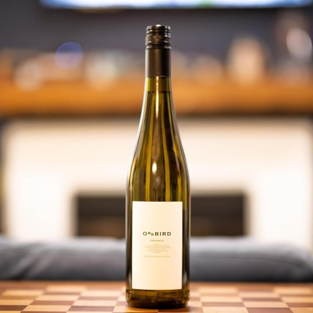 Oddbird Presence White Wine bottle placed on a checkered table with a cozy fireplace in the background