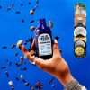 All The Bitter Aromatic Bitters bottle with award medals and floating spices on blue background
