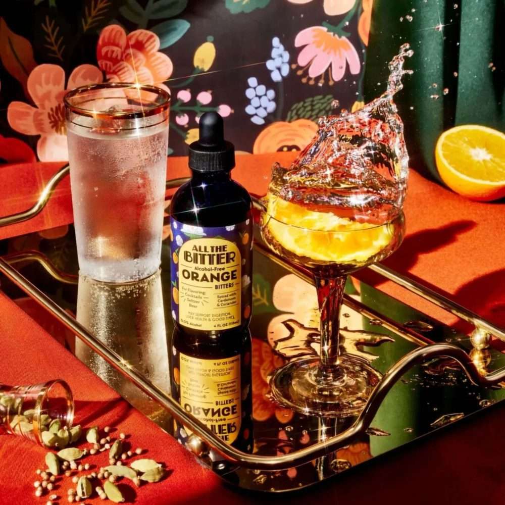 All The Bitter Orange Bitters bottle with sparkling cocktail splash, ice glass, and spices